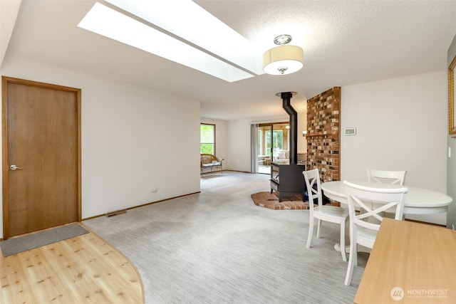 dining space with a wood stove, a skylight, a textured ceiling, wood finished floors, and baseboards