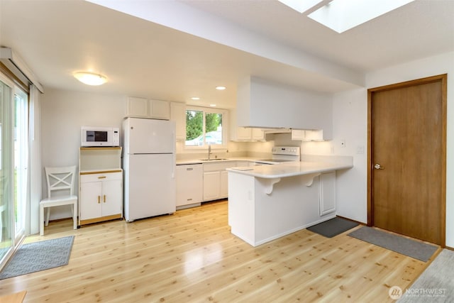 kitchen with white appliances, a peninsula, light wood-style flooring, light countertops, and recessed lighting