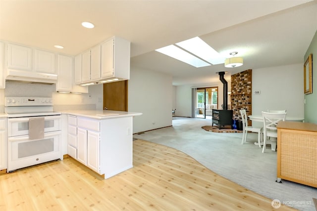 kitchen featuring under cabinet range hood, range with two ovens, a wood stove, light countertops, and light wood-type flooring