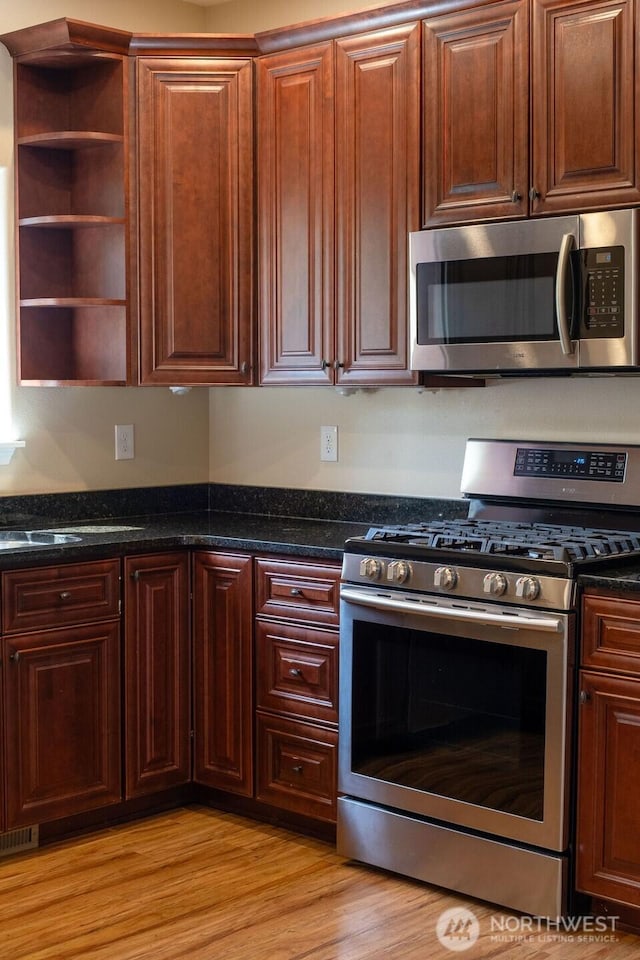 kitchen featuring appliances with stainless steel finishes, open shelves, dark stone counters, and light wood-type flooring