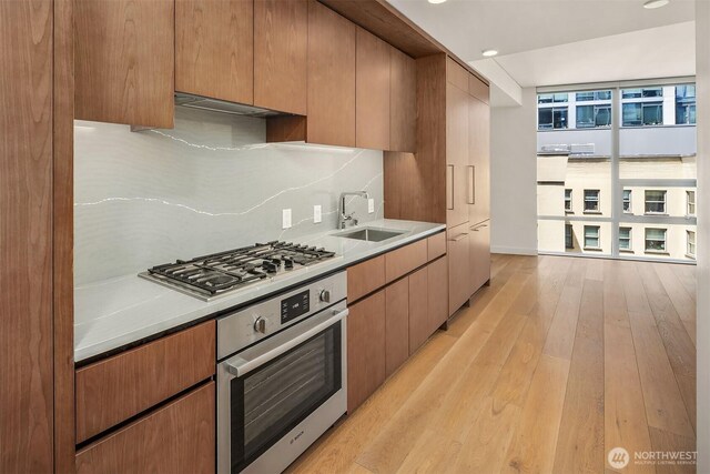 121 Stewart St Unit 908, Seattle, WA 98101 - kitchen with appliances with stainless steel finishes, a sink, light wood-style flooring, ventilation hood, and tasteful backsplash