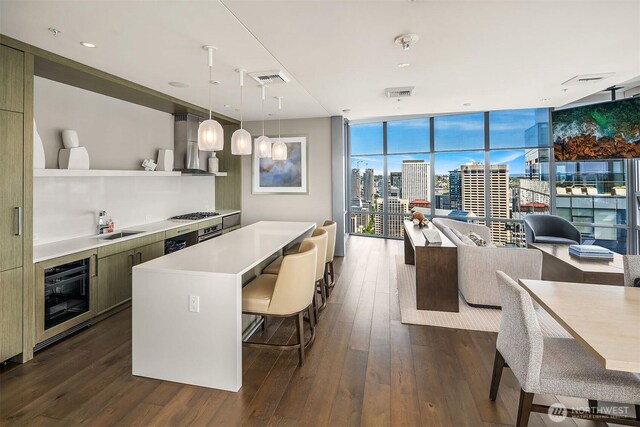 121 Stewart St Unit 908, Seattle, WA 98101 - kitchen with wall chimney range hood, oven, expansive windows, dark wood-style flooring, and a kitchen bar