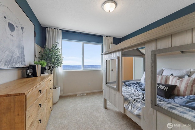 bedroom featuring light carpet, baseboards, a water view, and a textured ceiling