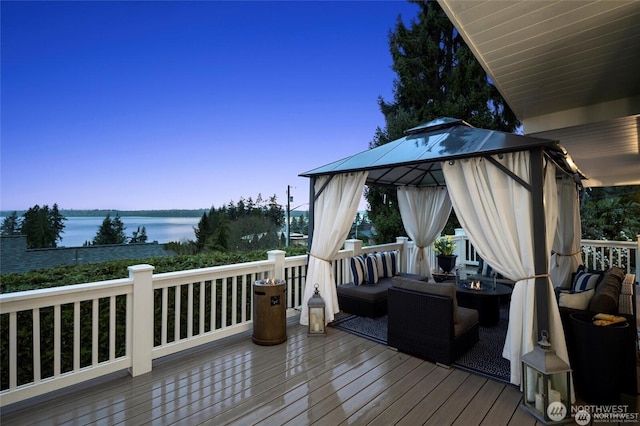 wooden deck with a gazebo, a water view, and an outdoor living space with a fire pit