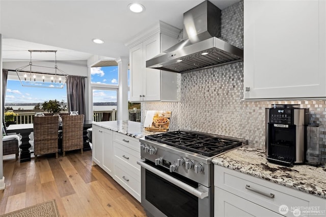 kitchen with wall chimney exhaust hood, high end stainless steel range, backsplash, white cabinets, and light wood finished floors