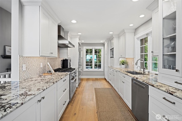 kitchen featuring stainless steel appliances, a sink, wall chimney range hood, white cabinets, and light wood finished floors