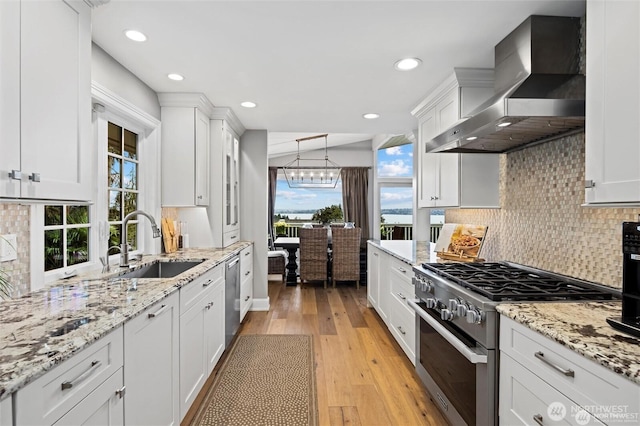 kitchen with appliances with stainless steel finishes, wall chimney range hood, a sink, backsplash, and plenty of natural light