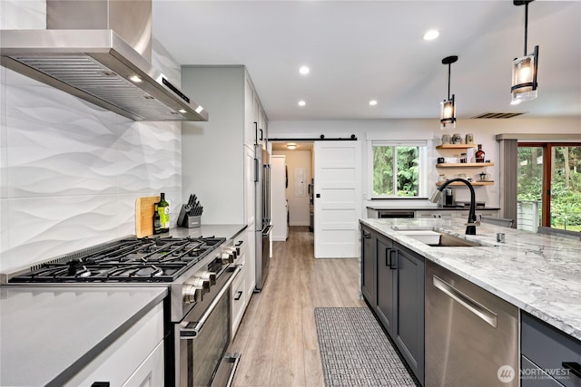 30 Hemlock Ct, Port Townsend, WA 98368 - kitchen with wall chimney range hood, stainless steel appliances, a barn door, recessed lighting, and light stone counters