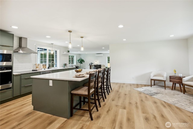 3598 Breeze Way NW, Bremerton, WA 98312 - kitchen featuring wall chimney range hood, appliances with stainless steel finishes, light countertops, a center island, and light wood-style flooring