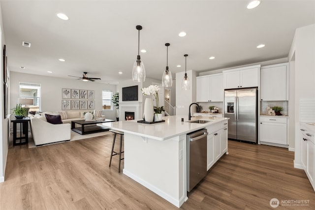 20307 145th St E Unit 860, Bonney Lake, WA 98391 - kitchen featuring appliances with stainless steel finishes, a warm lit fireplace, open floor plan, a sink, and white cabinets