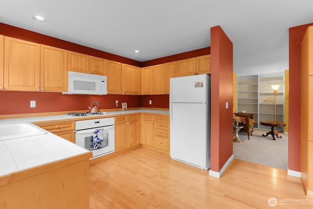 kitchen featuring white appliances, light brown cabinets, a sink, light wood-type flooring, and recessed lighting