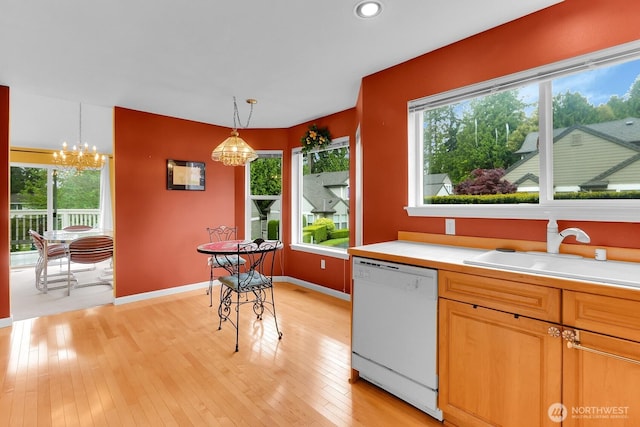 kitchen with white dishwasher, a sink, a chandelier, light wood-style floors, and pendant lighting
