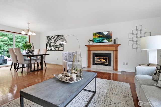 living area featuring a chandelier, a tile fireplace, wood finished floors, and baseboards