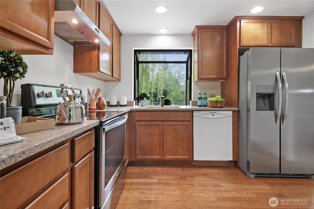 kitchen featuring appliances with stainless steel finishes, ventilation hood, a sink, brown cabinetry, and light wood-style floors