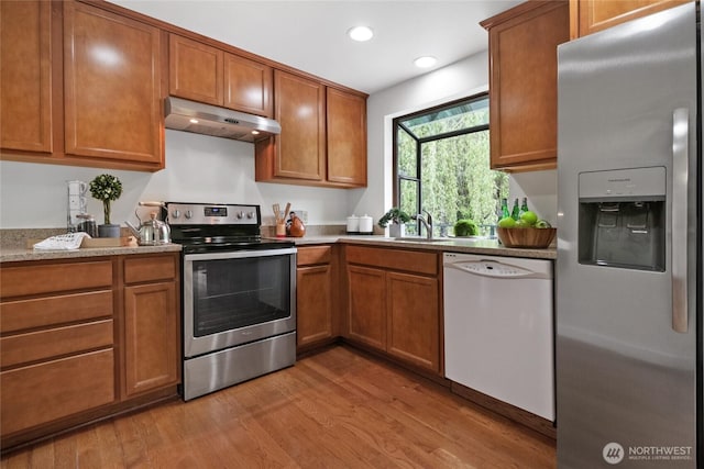 kitchen featuring stainless steel appliances, under cabinet range hood, light wood-style flooring, brown cabinets, and recessed lighting