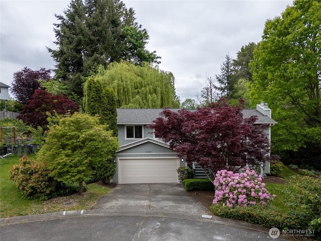 view of property hidden behind natural elements with driveway, a chimney, a garage, and stairs