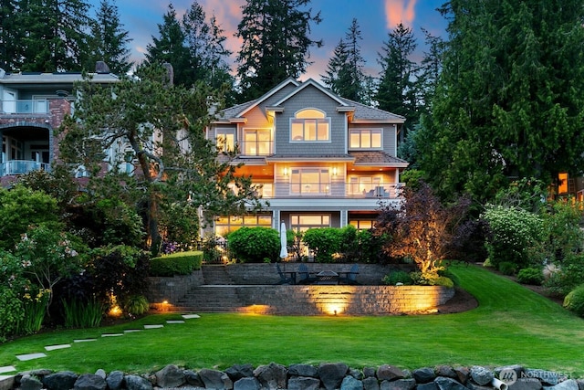 back of house at dusk featuring a yard and a balcony