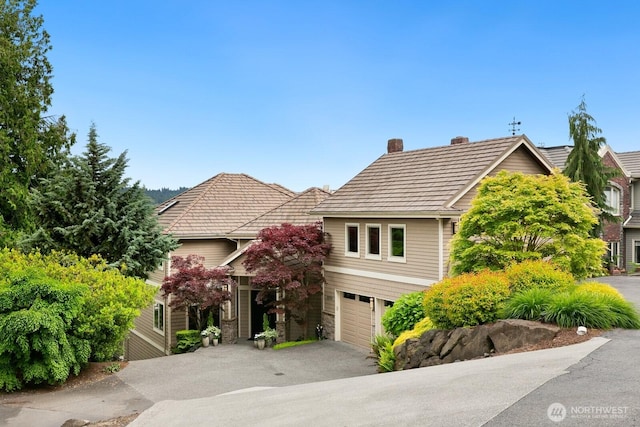 view of front of home featuring a chimney, driveway, an attached garage, and a tiled roof