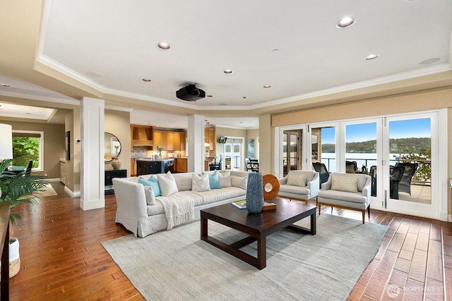 living room featuring light wood-style floors, ornamental molding, a raised ceiling, a water view, and recessed lighting