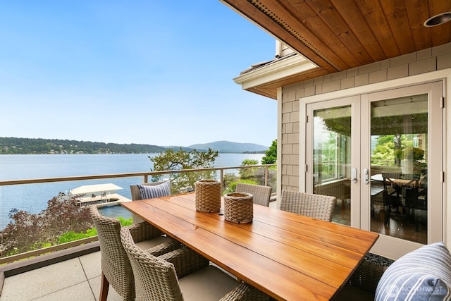 balcony with a water and mountain view, outdoor dining space, and french doors
