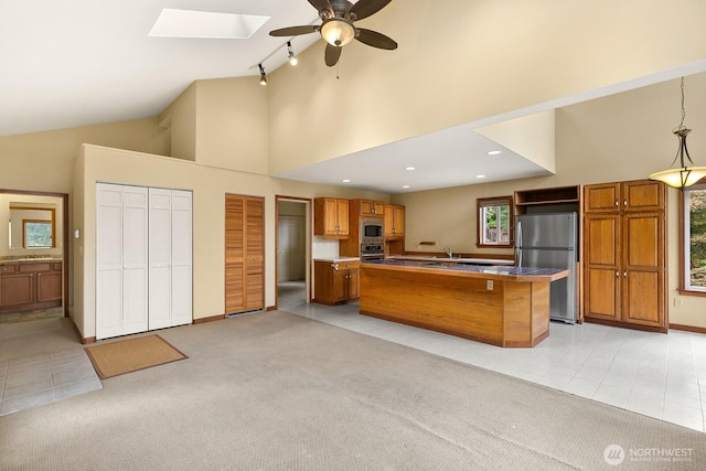 kitchen featuring stainless steel appliances, brown cabinetry, a ceiling fan, a skylight, and light tile patterned floors