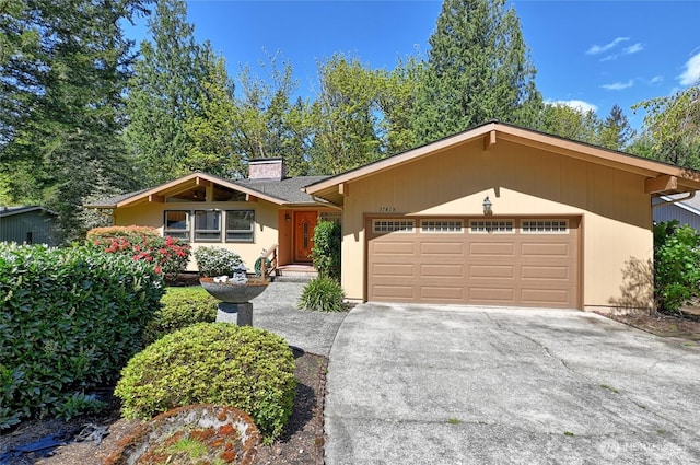 mid-century home with an attached garage, concrete driveway, and a chimney