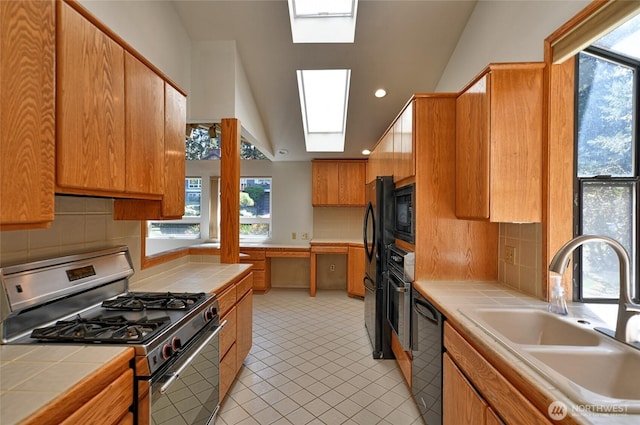 kitchen with black appliances, tile countertops, a sink, healthy amount of natural light, and vaulted ceiling