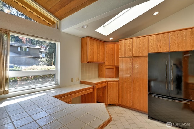 kitchen with freestanding refrigerator, tile countertops, lofted ceiling, a skylight, and healthy amount of natural light
