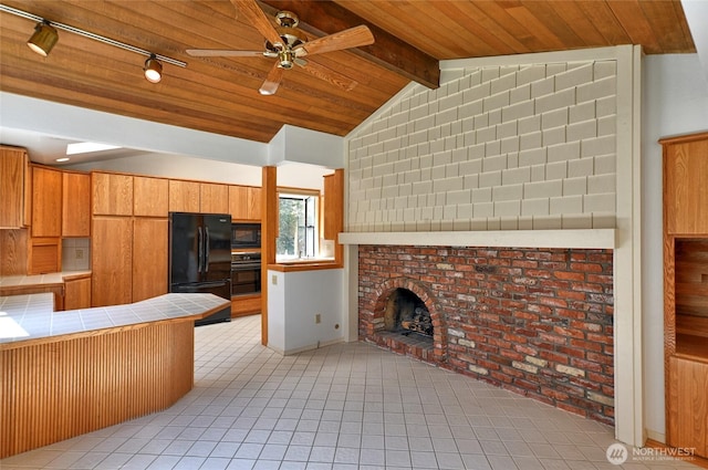 kitchen with black appliances, tile counters, a ceiling fan, light tile patterned flooring, and a brick fireplace