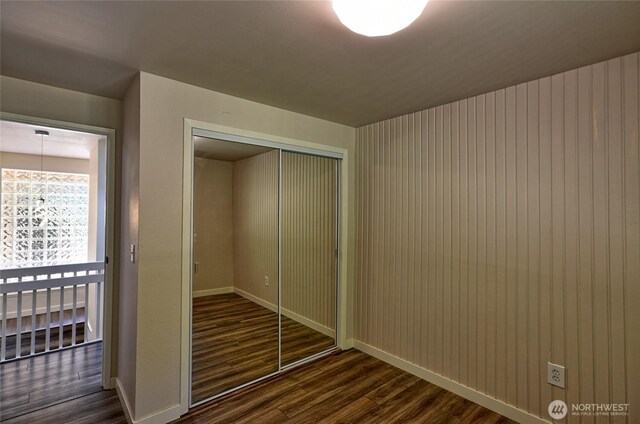 unfurnished bedroom featuring dark wood-style flooring, a closet, and baseboards