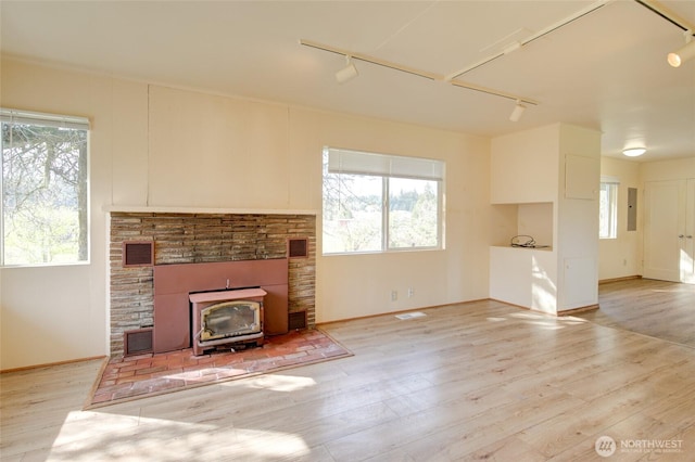 unfurnished living room with rail lighting, a wood stove, wood finished floors, and electric panel