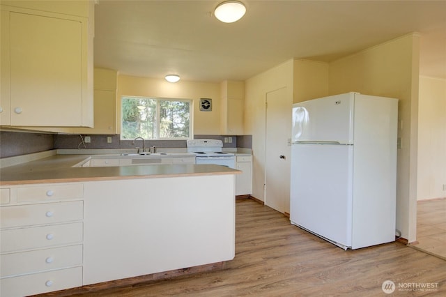 kitchen with white appliances, a sink, light countertops, a peninsula, and light wood-style floors