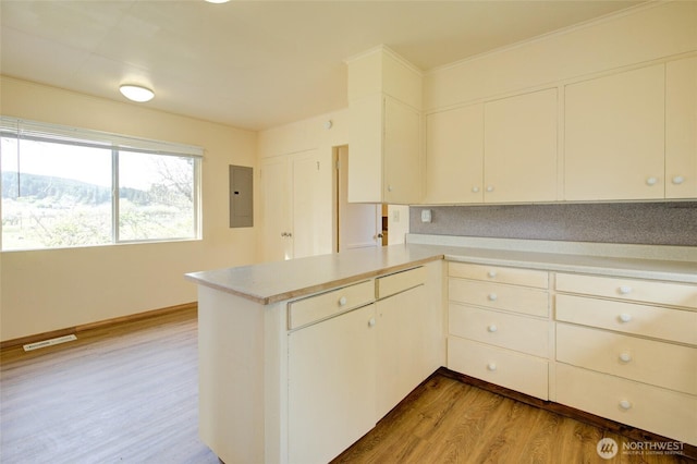 kitchen featuring a peninsula, light countertops, light wood-style flooring, and electric panel