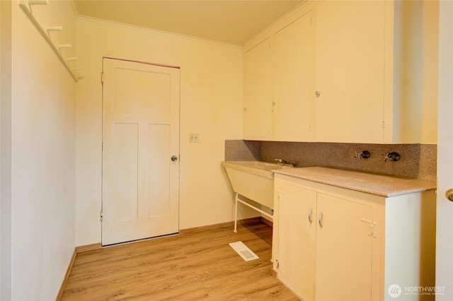 laundry room with ornamental molding, light wood-type flooring, and baseboards