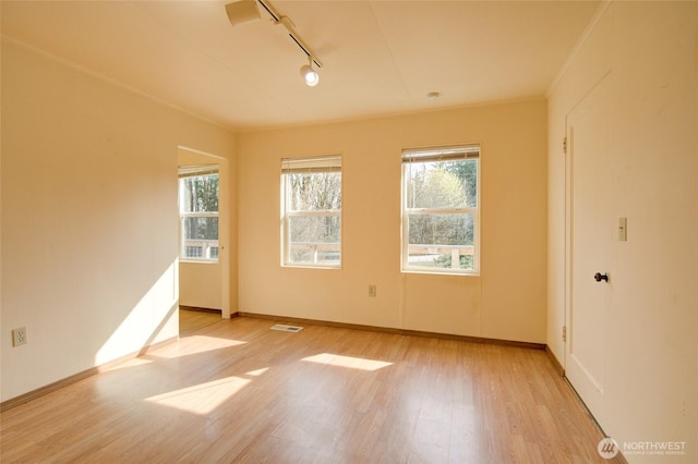 spare room featuring light wood finished floors, track lighting, baseboards, and ornamental molding