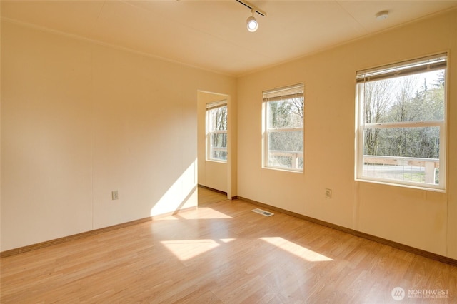 empty room featuring wood finished floors, rail lighting, and baseboards