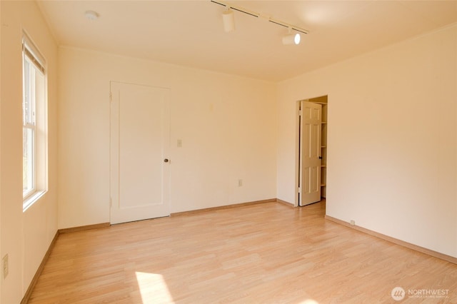 empty room featuring track lighting, light wood-type flooring, and baseboards