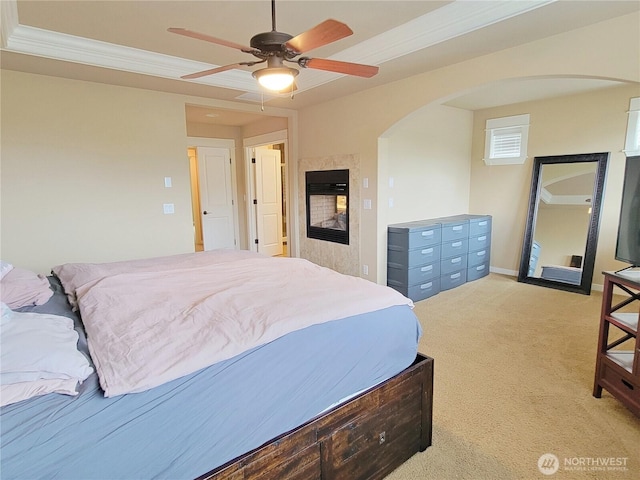 bedroom featuring arched walkways, light carpet, a tiled fireplace, crown molding, and a ceiling fan