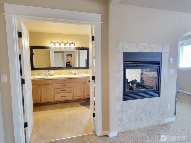 bathroom with a fireplace, double vanity, baseboards, and backsplash