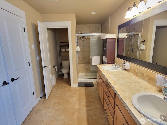 bathroom featuring a stall shower, double vanity, toilet, backsplash, and baseboards