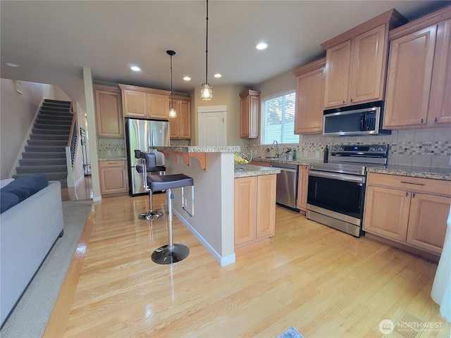 kitchen with appliances with stainless steel finishes, light wood finished floors, a kitchen breakfast bar, tasteful backsplash, and recessed lighting