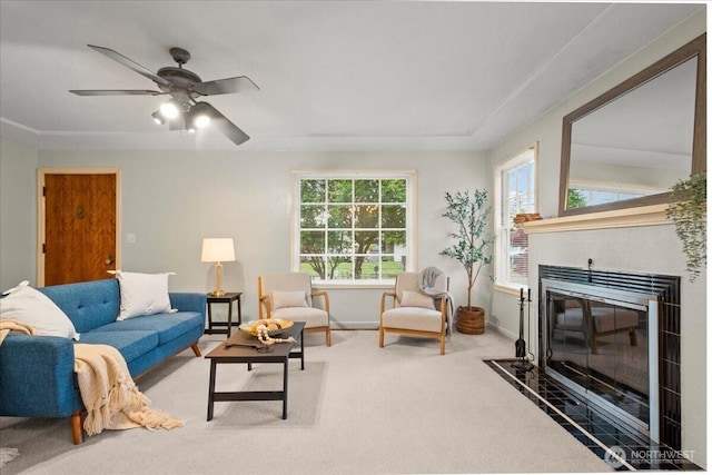 living area featuring a tile fireplace, carpet, baseboards, and ceiling fan