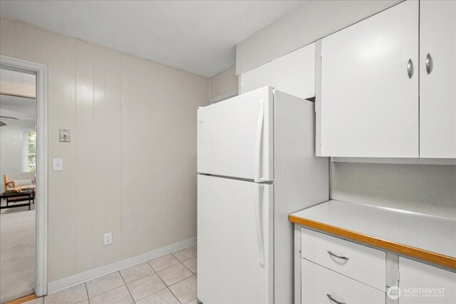 kitchen featuring freestanding refrigerator, white cabinetry, light countertops, light tile patterned floors, and baseboards
