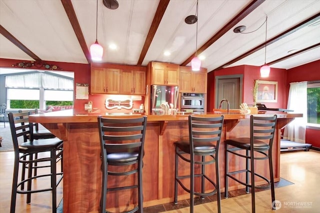 kitchen with appliances with stainless steel finishes, hanging light fixtures, a large island with sink, recessed lighting, and a breakfast bar