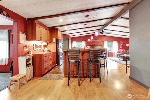 kitchen featuring freestanding refrigerator, light wood finished floors, a kitchen breakfast bar, and brown cabinets