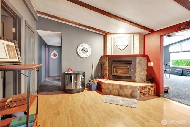 living room featuring beamed ceiling, a stone fireplace, and wood finished floors