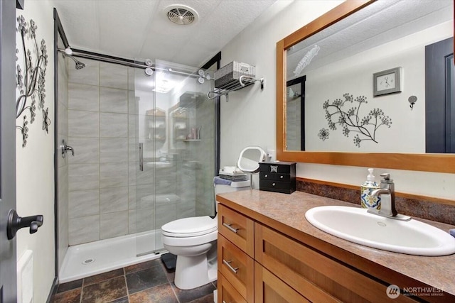 bathroom featuring a stall shower, toilet, vanity, and stone finish flooring