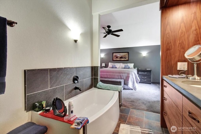 ensuite bathroom featuring ceiling fan, a bath, vanity, and stone finish flooring