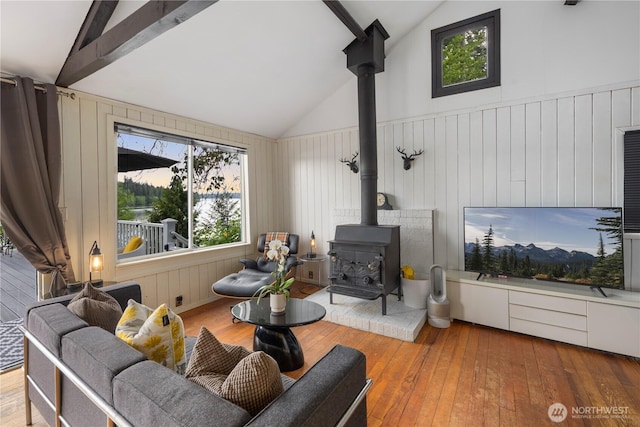 living area featuring a wood stove, plenty of natural light, hardwood / wood-style flooring, high vaulted ceiling, and beamed ceiling