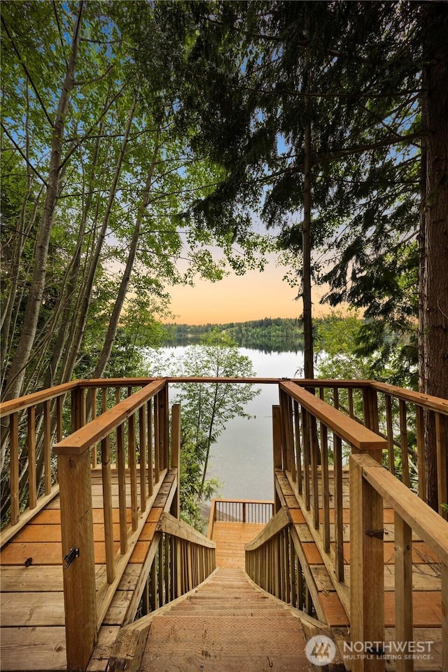 deck at dusk featuring a water view and stairway